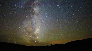 An image of the Milky Way Galaxy at night, with rocks in silhouette in the foreground.